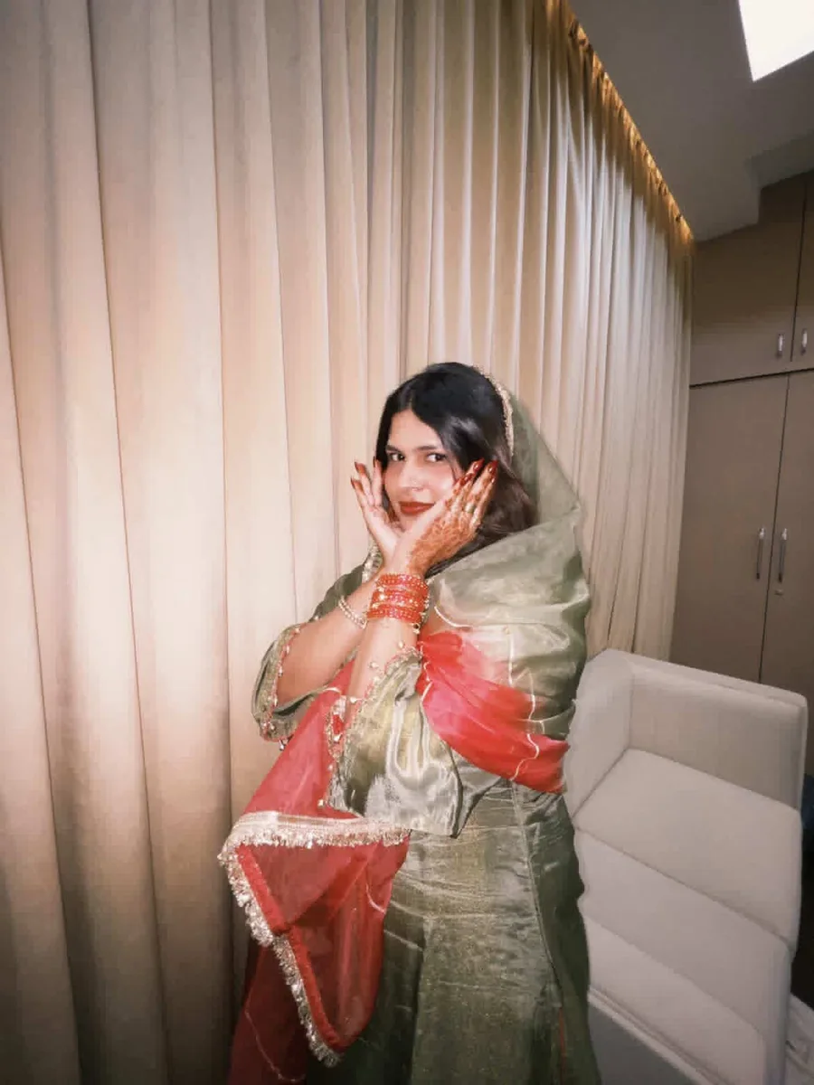 Shiza in a sage-green outfit with a coral dupatta, hands framing her face